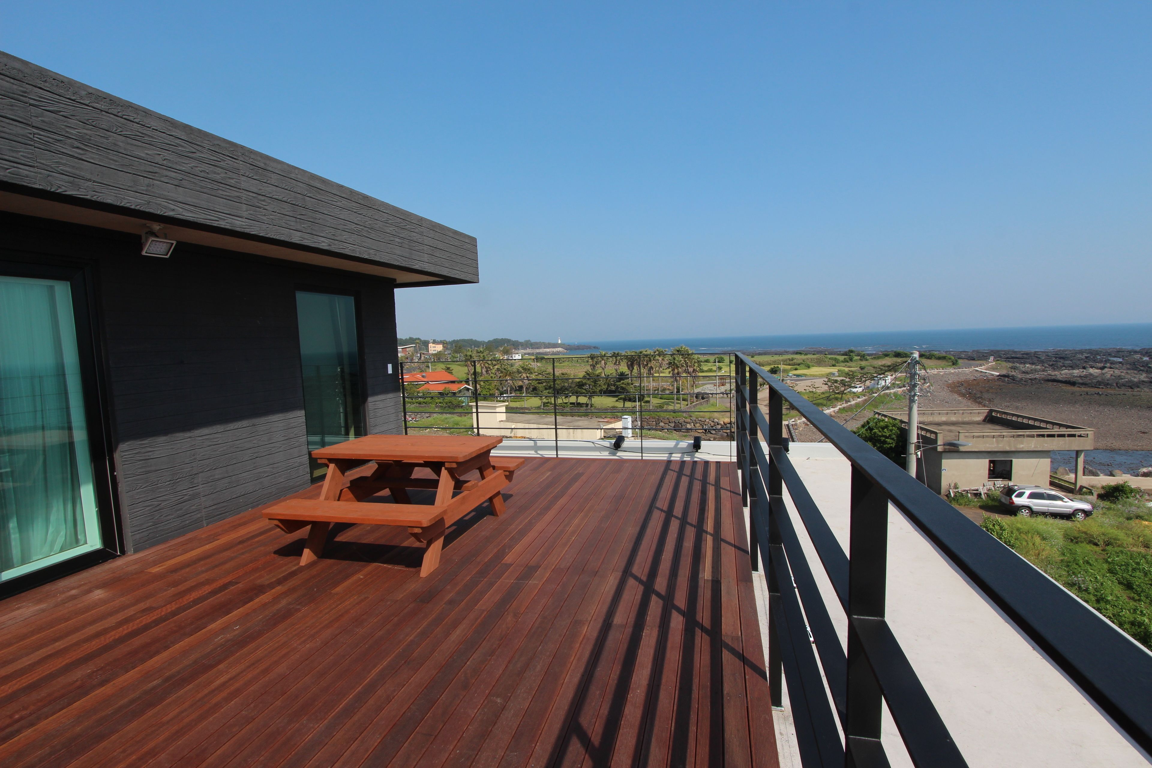 Un terrazzo in legno con tavolo da picnic, un balcone con ringhiera e vista sull'oceano e su edifici in lontananza.