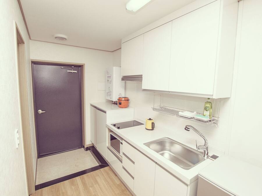 A compact kitchen with white cabinets, a stainless steel sink, a microwave, and a small orange appliance on the countertop.
