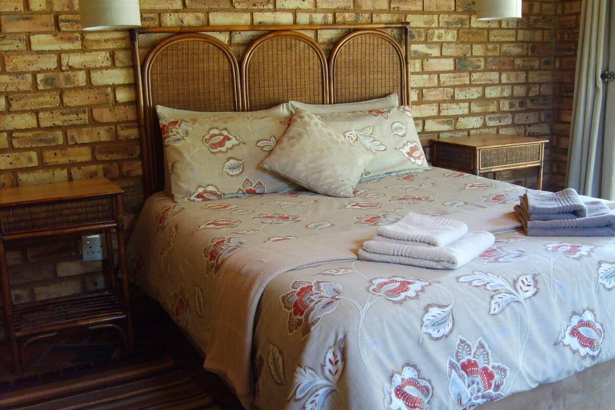 Une chambre avec un mur en briques, une tête de lit en bois, une literie à motifs floraux et deux tables de chevet avec des lampes.