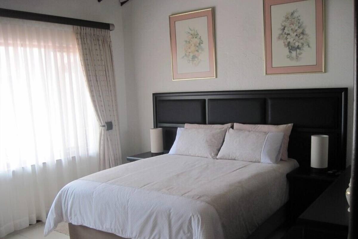 A bedroom with a large bed, two bedside tables, and a window with curtains.