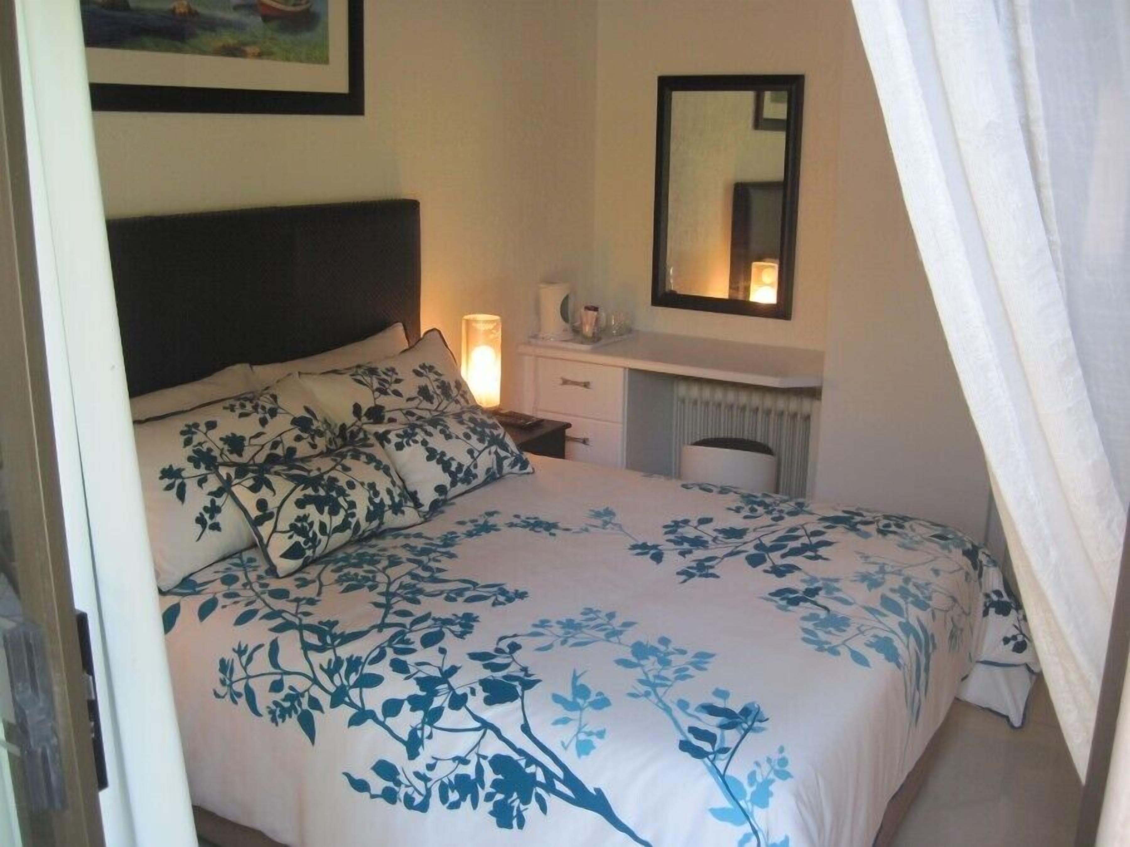 A bedroom with a bed, a nightstand, a dresser, a mirror, and a radiator.
