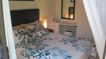 A bedroom with a bed, a nightstand, a dresser, a mirror, and a radiator.