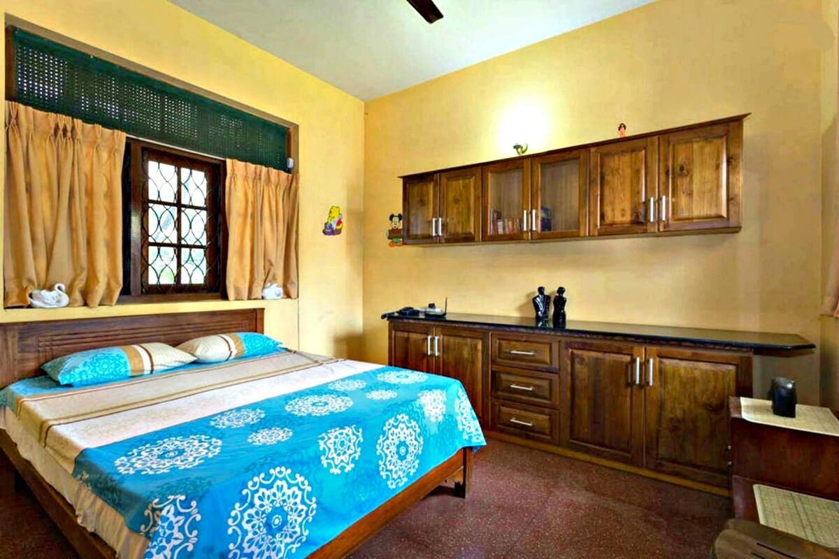 A bedroom with a bed, a window with curtains, wooden cabinets, and a small desk.