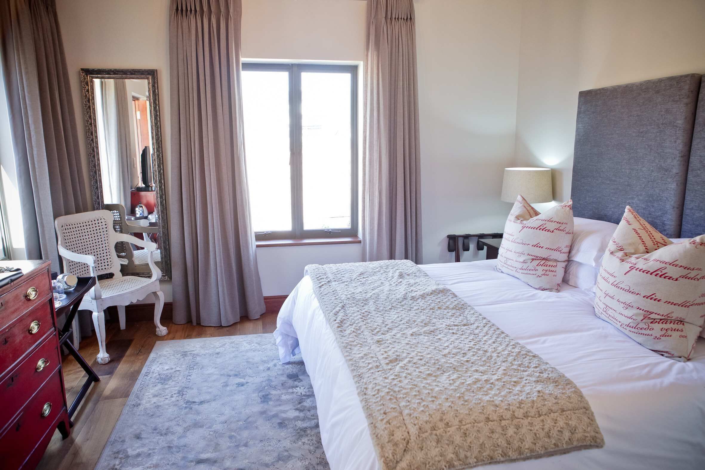 Une chambre d’hôtel comprenant un lit, un bureau, une chaise, une commode et une fenêtre avec des rideaux.