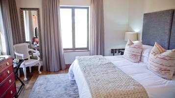 Une chambre d’hôtel comprenant un lit, un bureau, une chaise, une commode et une fenêtre avec des rideaux.