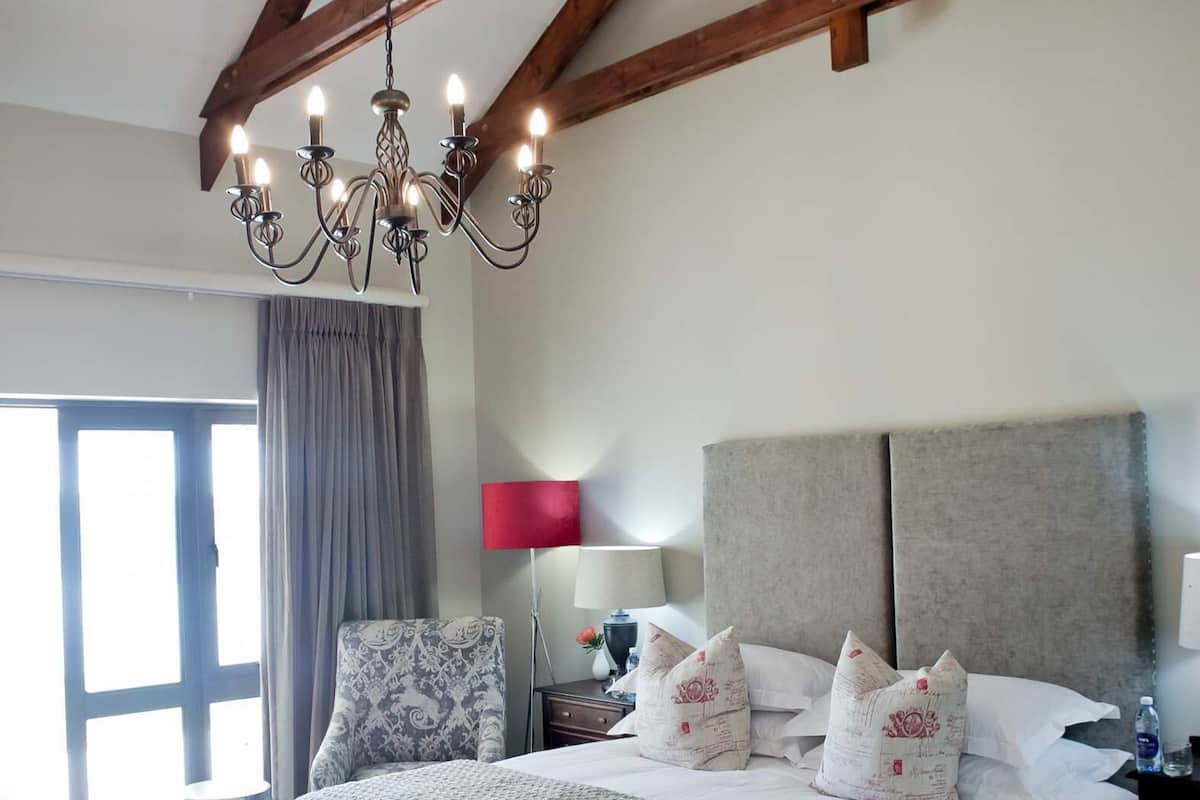 A bedroom with a large bed, a chandelier, a bench, and a nightstand.