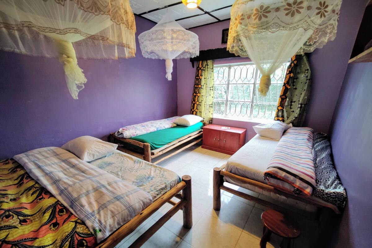 A room with two wooden beds, a red cabinet, and a window with decorative curtains.