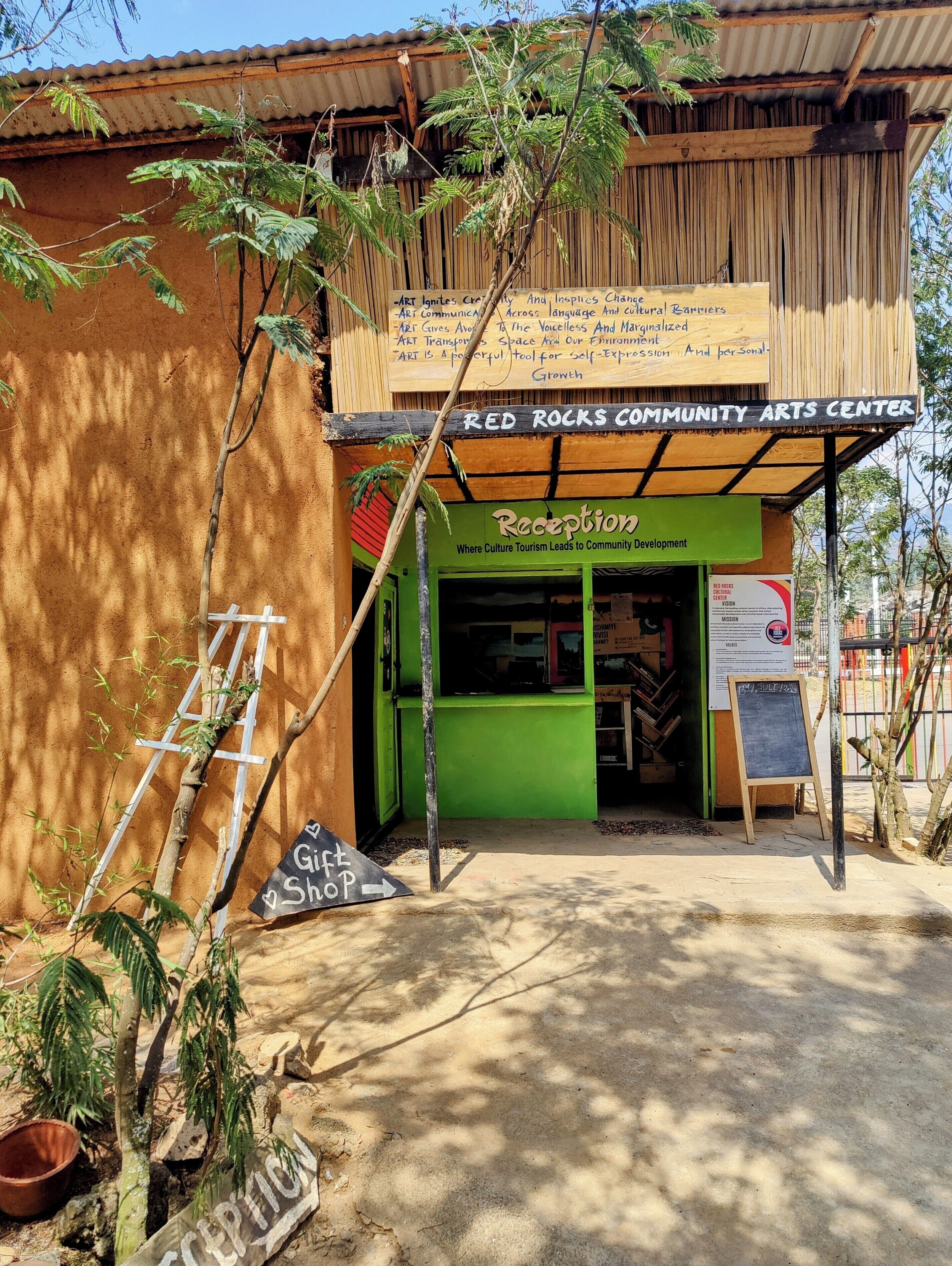 Um centro de artes comunitário com área de recepção, placa indicando uma loja de presentes e uma lousa com escrita.