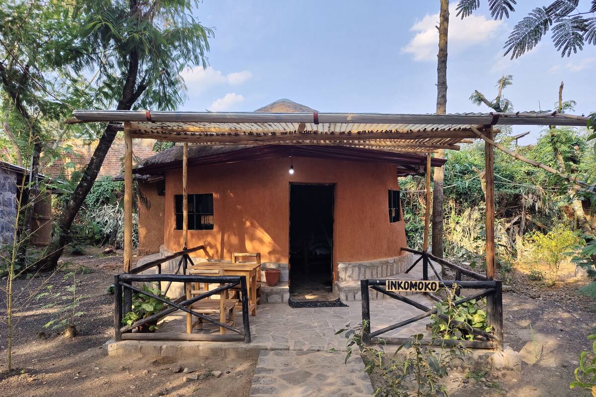 A rustic house with a thatched roof, a wooden porch, and a stone pathway leading to the entrance.