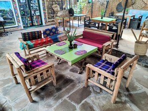 A rustic outdoor seating area with wooden furniture and colorful cushions, surrounded by stone flooring and a decorative wall.