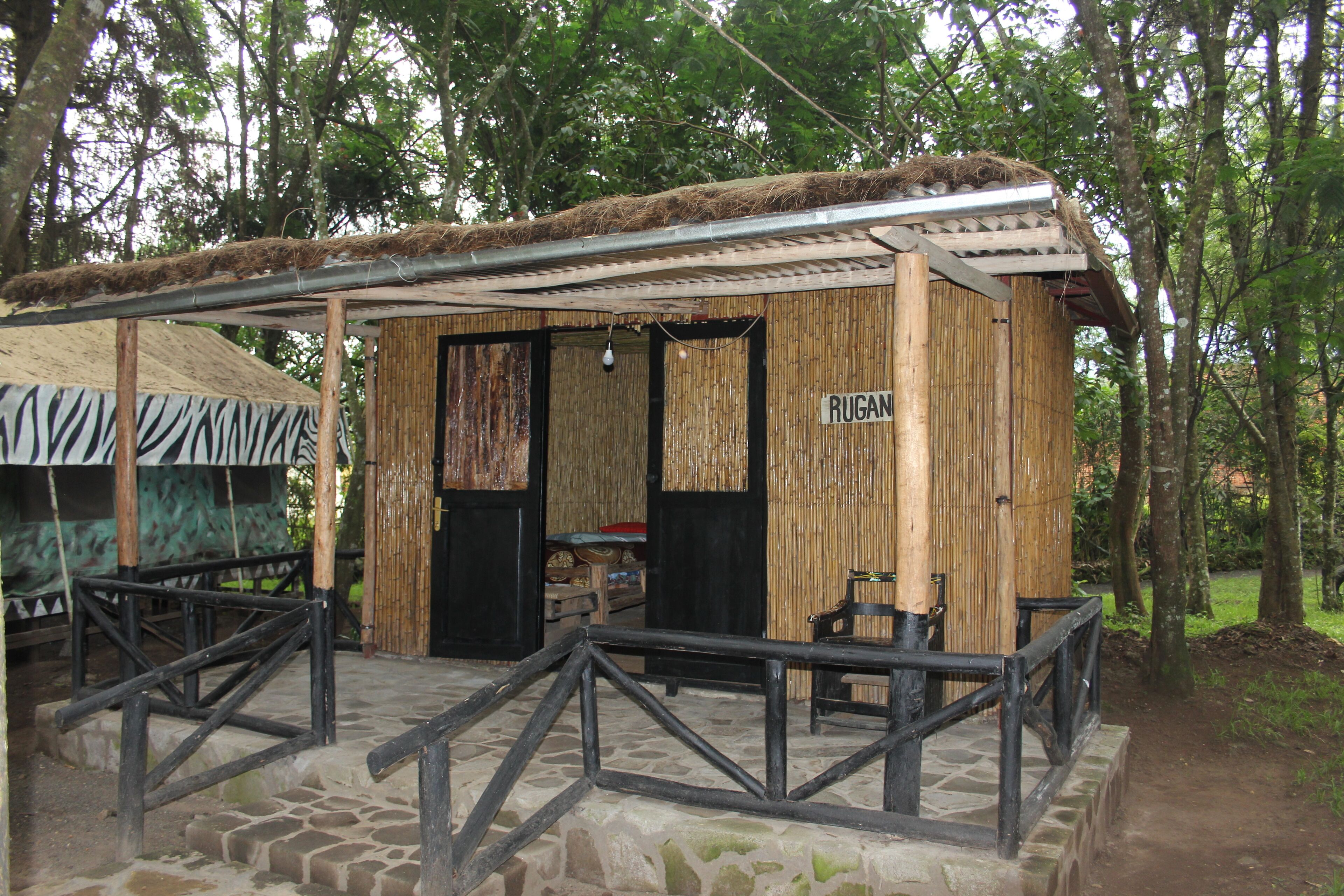 A rustic wooden structure with a bamboo exterior, a sign reading "RUGAN," and a stone-paved entrance area.
