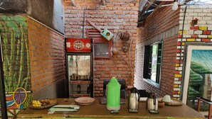 A narrow alley with a green counter, a refrigerator stocked with beverages, and a brick wall with colorful patches. - Red Rocks Rwanda Guesthouse & Campsite (Nkotsi)