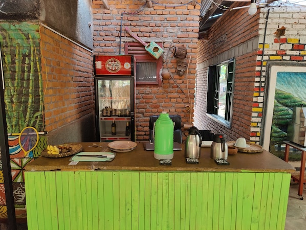 A narrow alley with a green counter, a refrigerator stocked with beverages, and a brick wall with colorful patches.