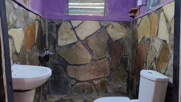 A bathroom with a stone wall, a toilet, and a sink.