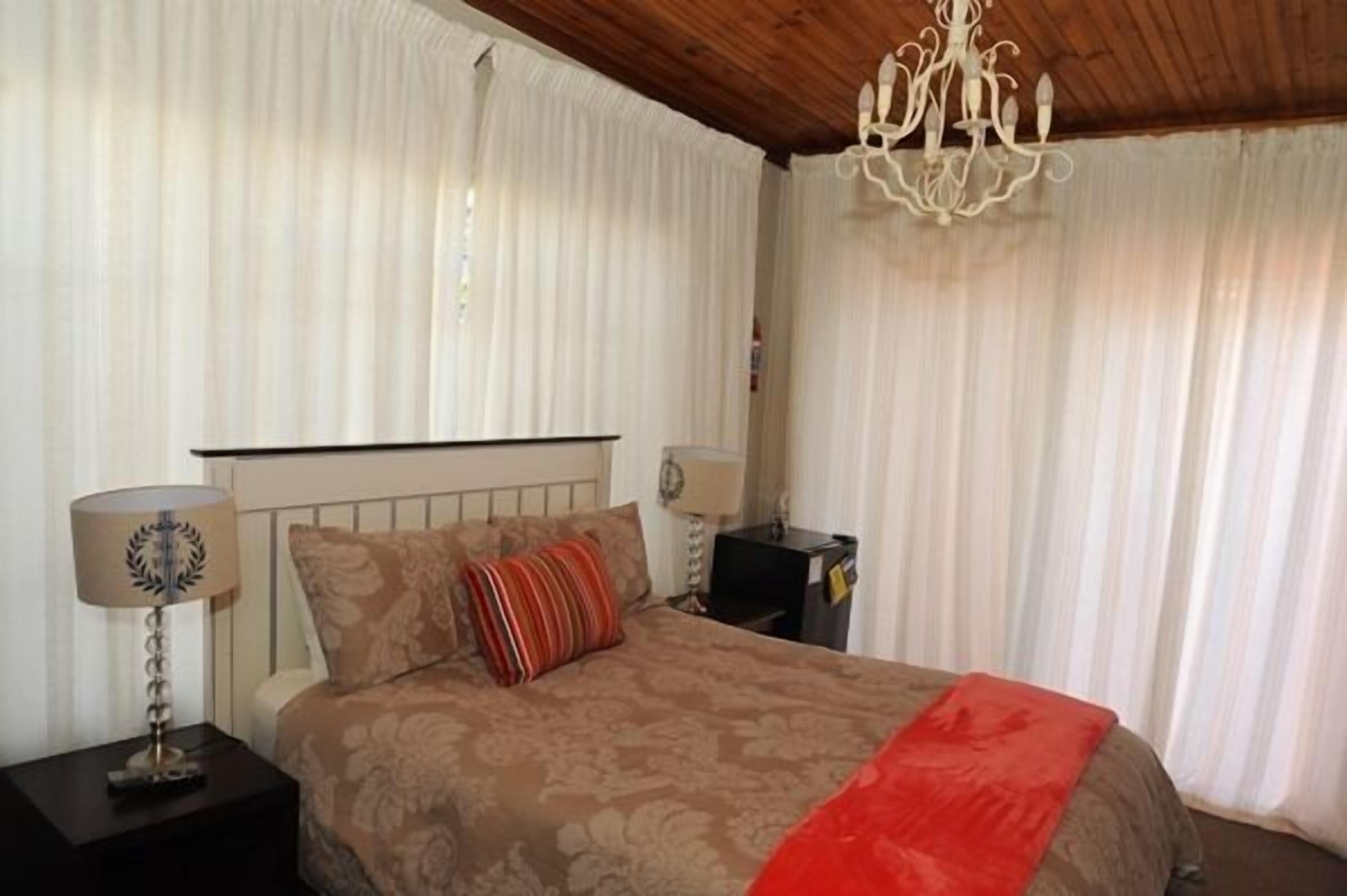 Une chambre à coucher avec un lit, deux tables de chevet, un lustre et des rideaux.