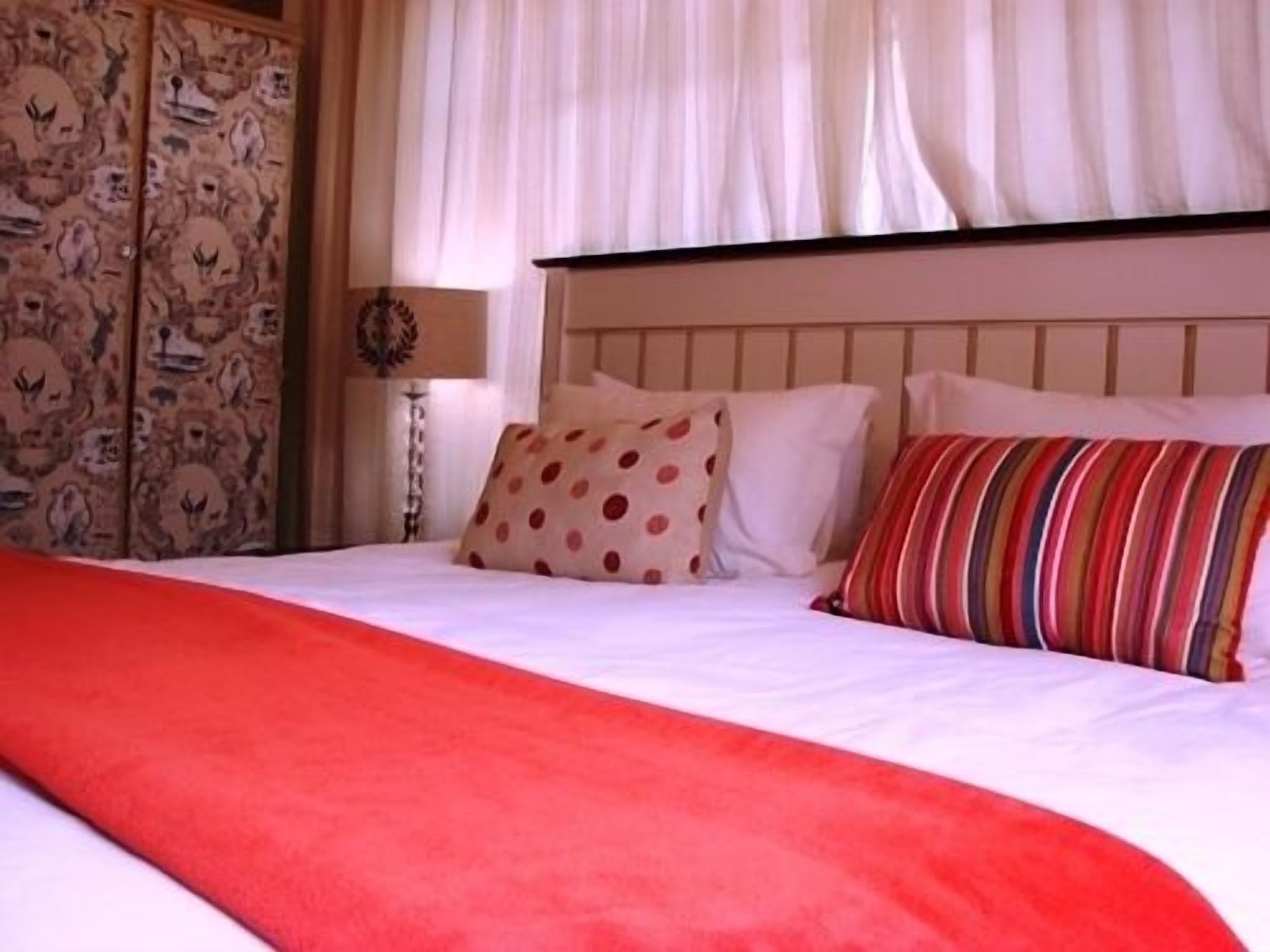 Una cama con una manta roja, almohadas blancas y una almohada a rayas.