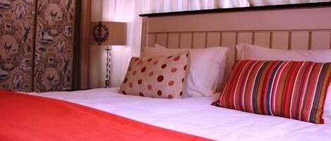 Una cama con una manta roja, almohadas blancas y una almohada a rayas.