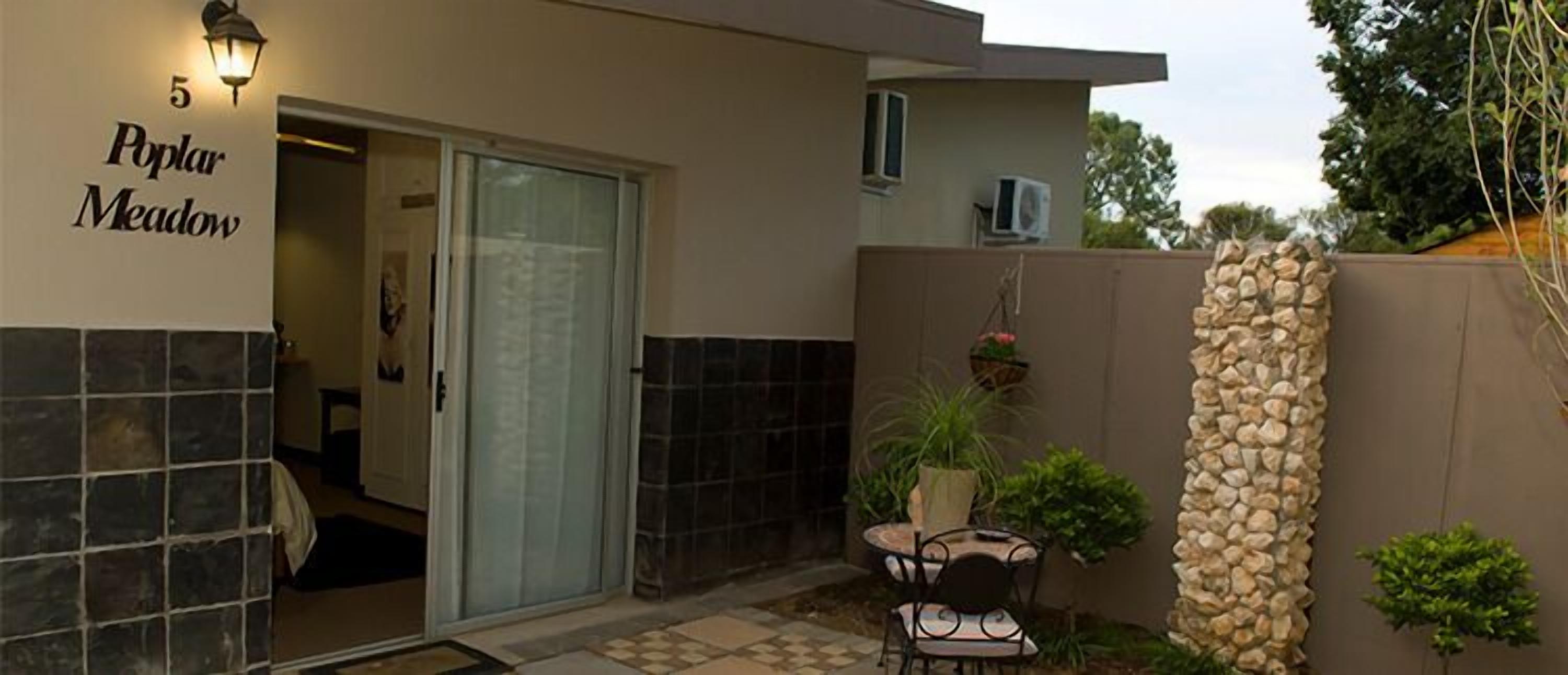 A modern building with a glass door entrance, a stone wall, and a small patio area with a table and chairs.