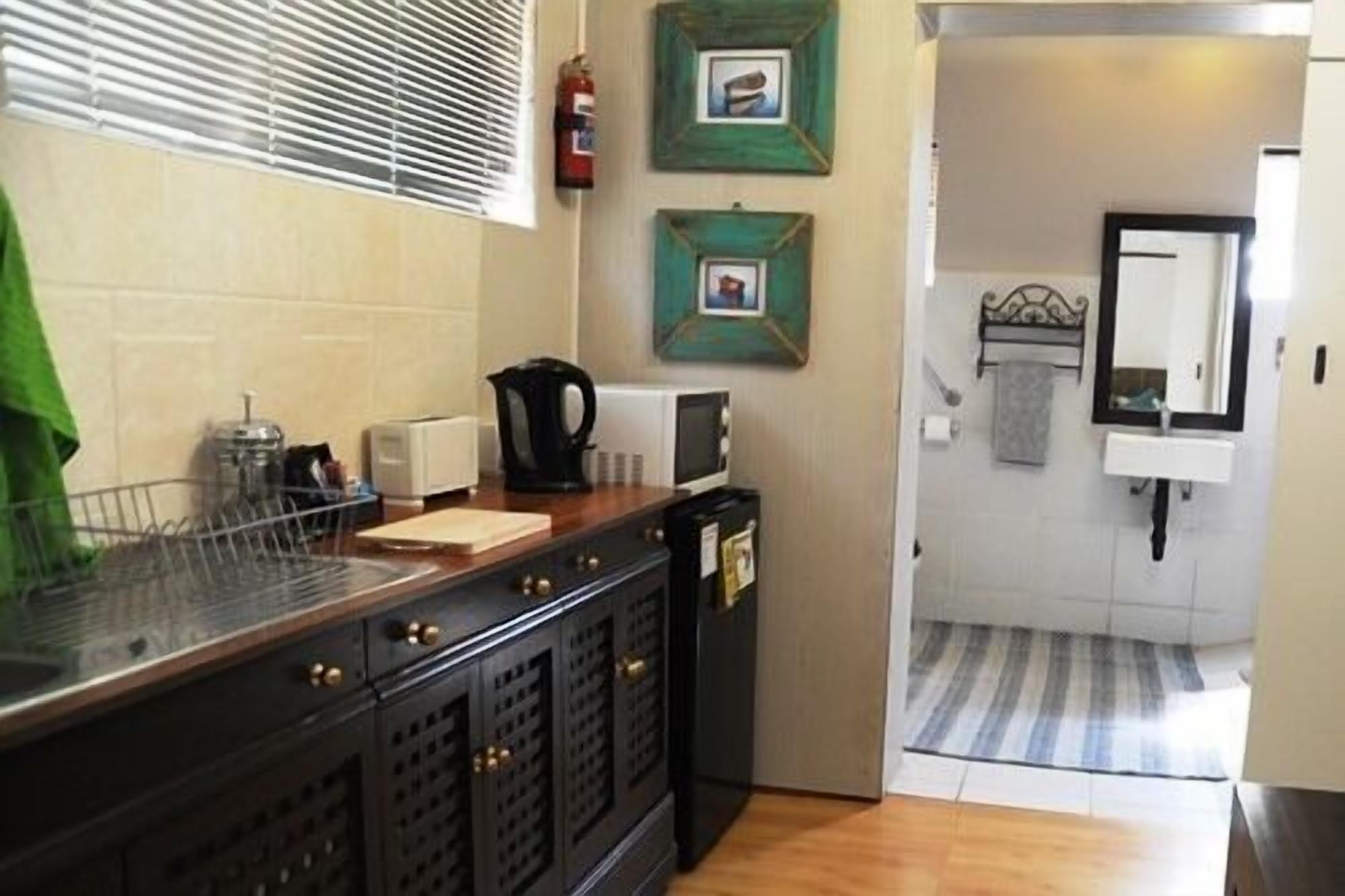 A kitchen with a wooden countertop, a kettle, a toaster, and a coffee maker. There are two framed pictures on the wall, a fire extinguisher, and a sink with a towel.