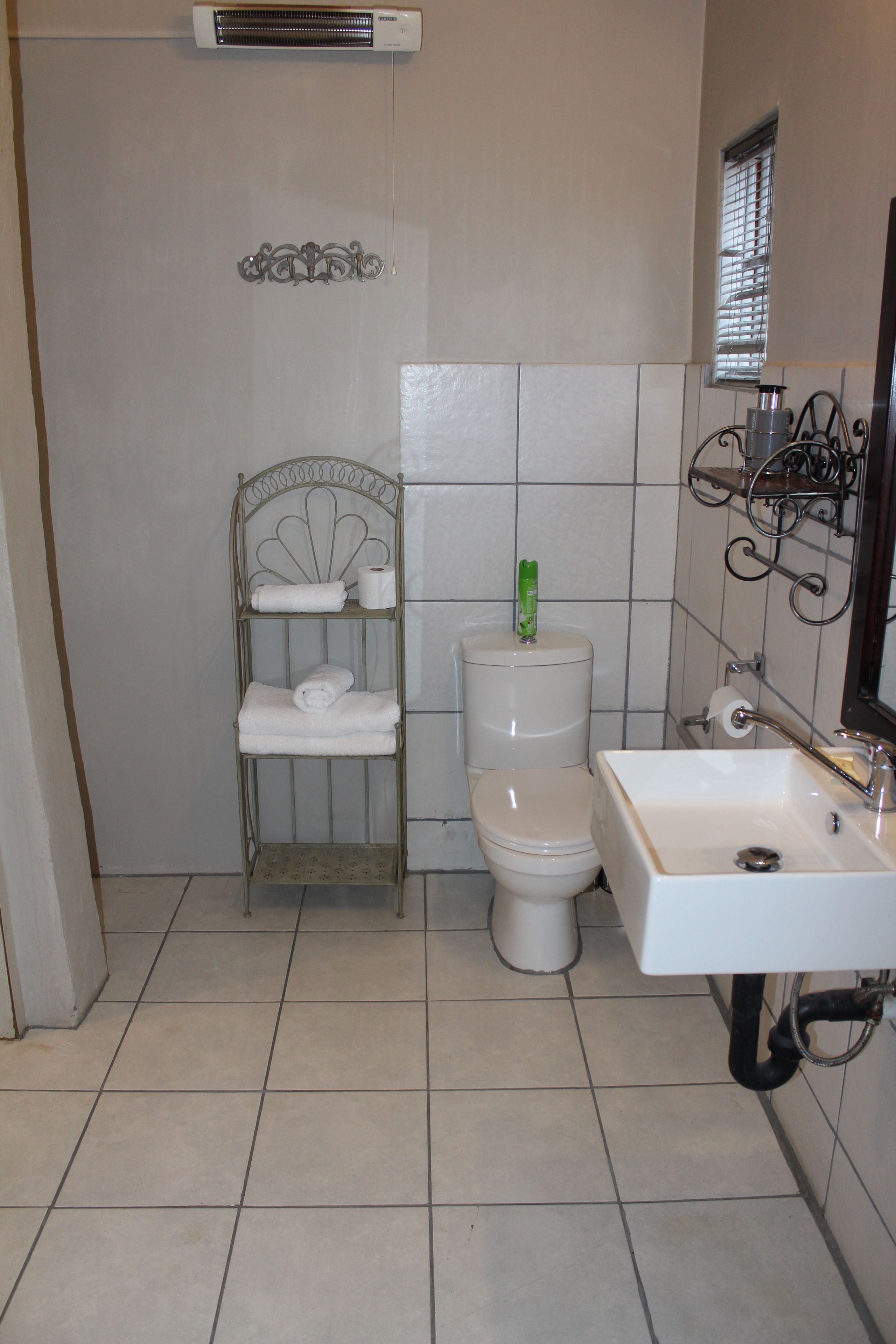 A bathroom with a toilet, a shelf with towels, a sink, and a window with blinds.