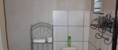 A bathroom with a toilet, a shelf with towels, a sink, and a window with blinds.