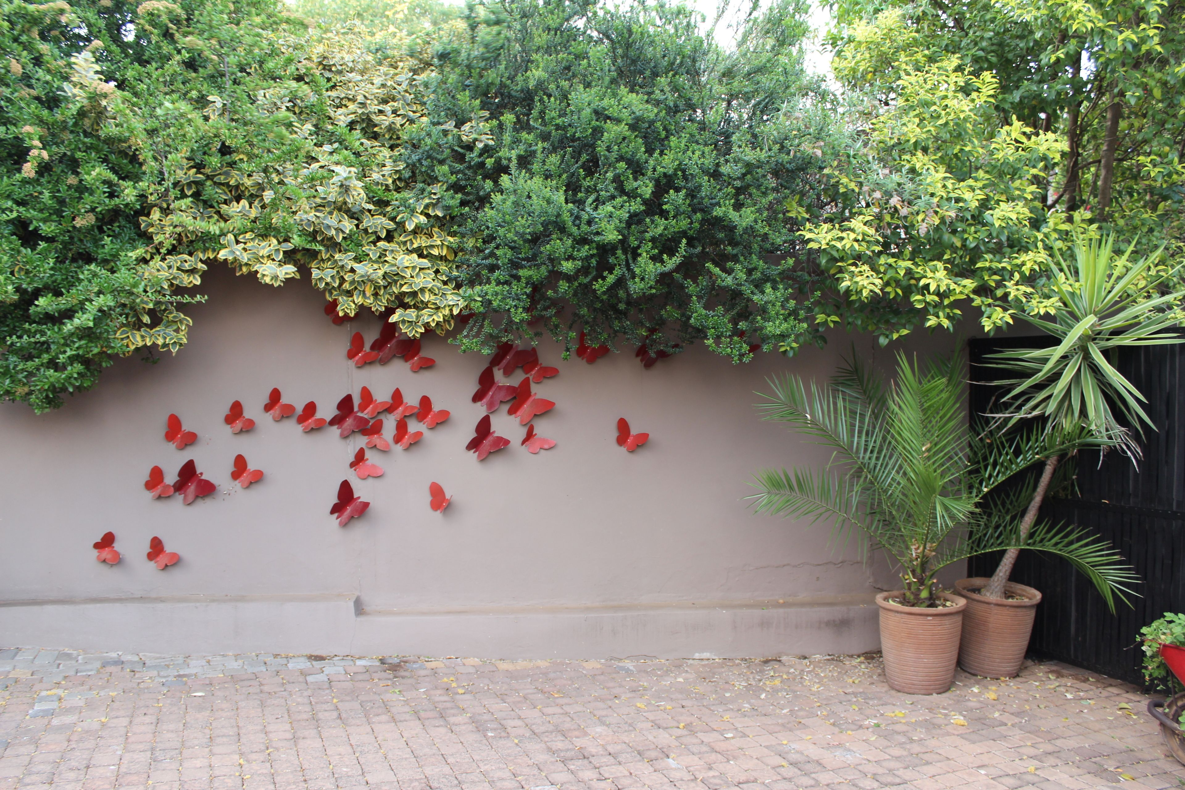 A wall with red butterfly decorations, a potted plant, and a brick-paved ground.
