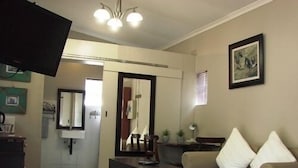 Una sala de estar con un sofá, una mesa de centro y un televisor. Se ve una puerta que da a otra habitación.