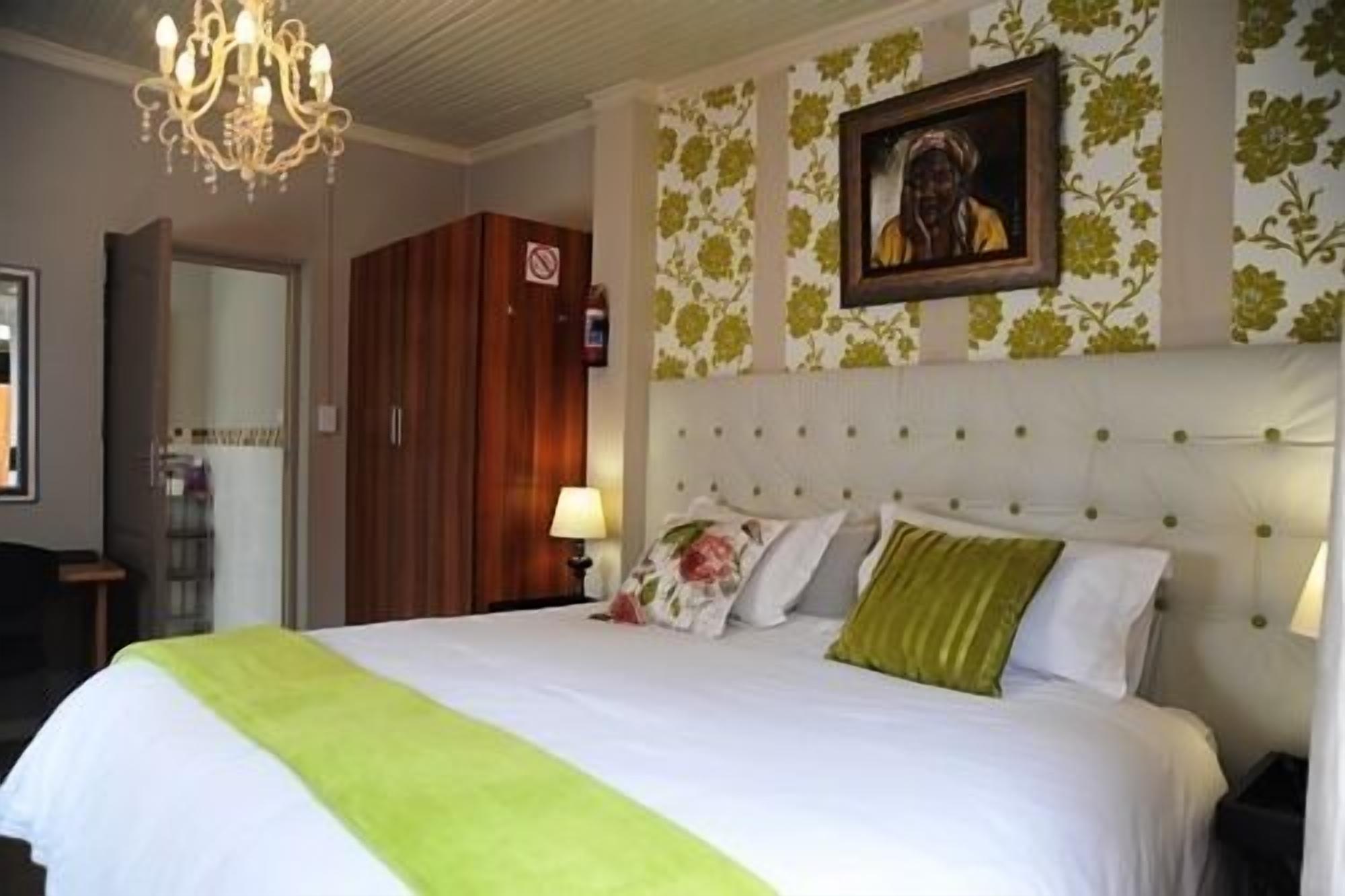 A hotel room with a large bed, a chandelier, a framed picture on the wall, and a wardrobe.