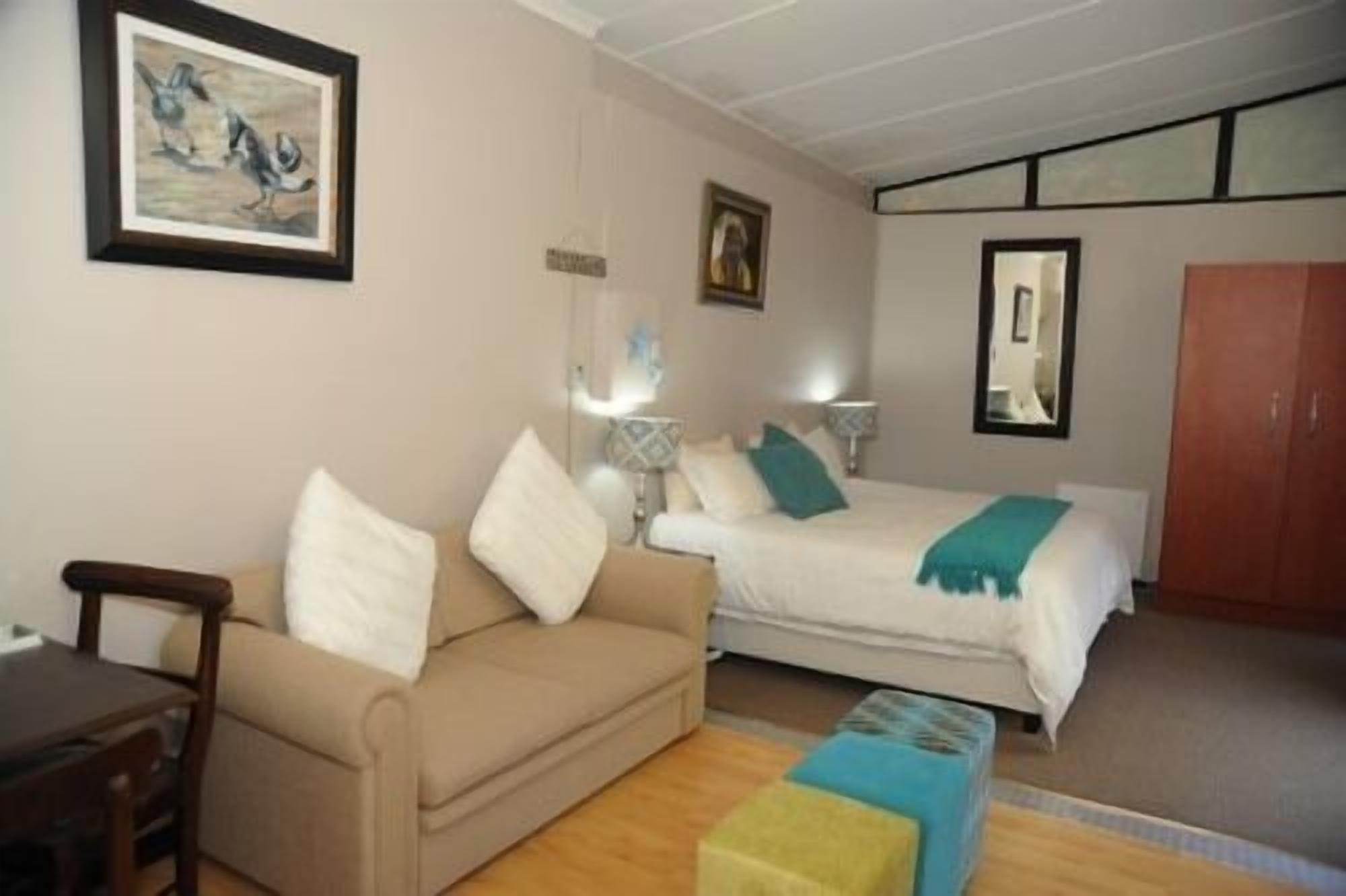 A hotel room with a bed, a sofa, a small table, and a painting on the wall.