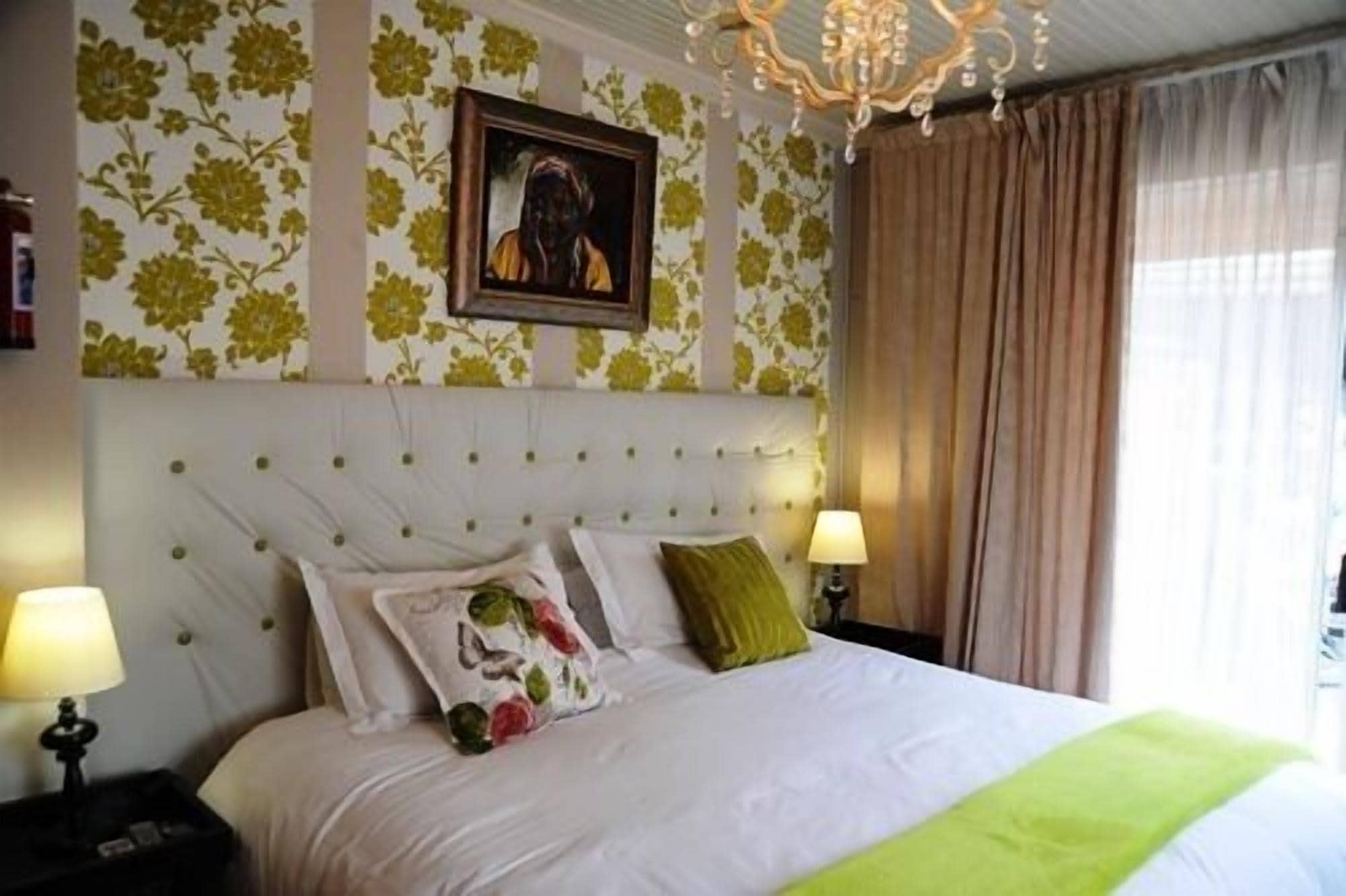 Una habitación de hotel con una cama grande, dos lámparas de noche, una araña y papel tapiz floral.
