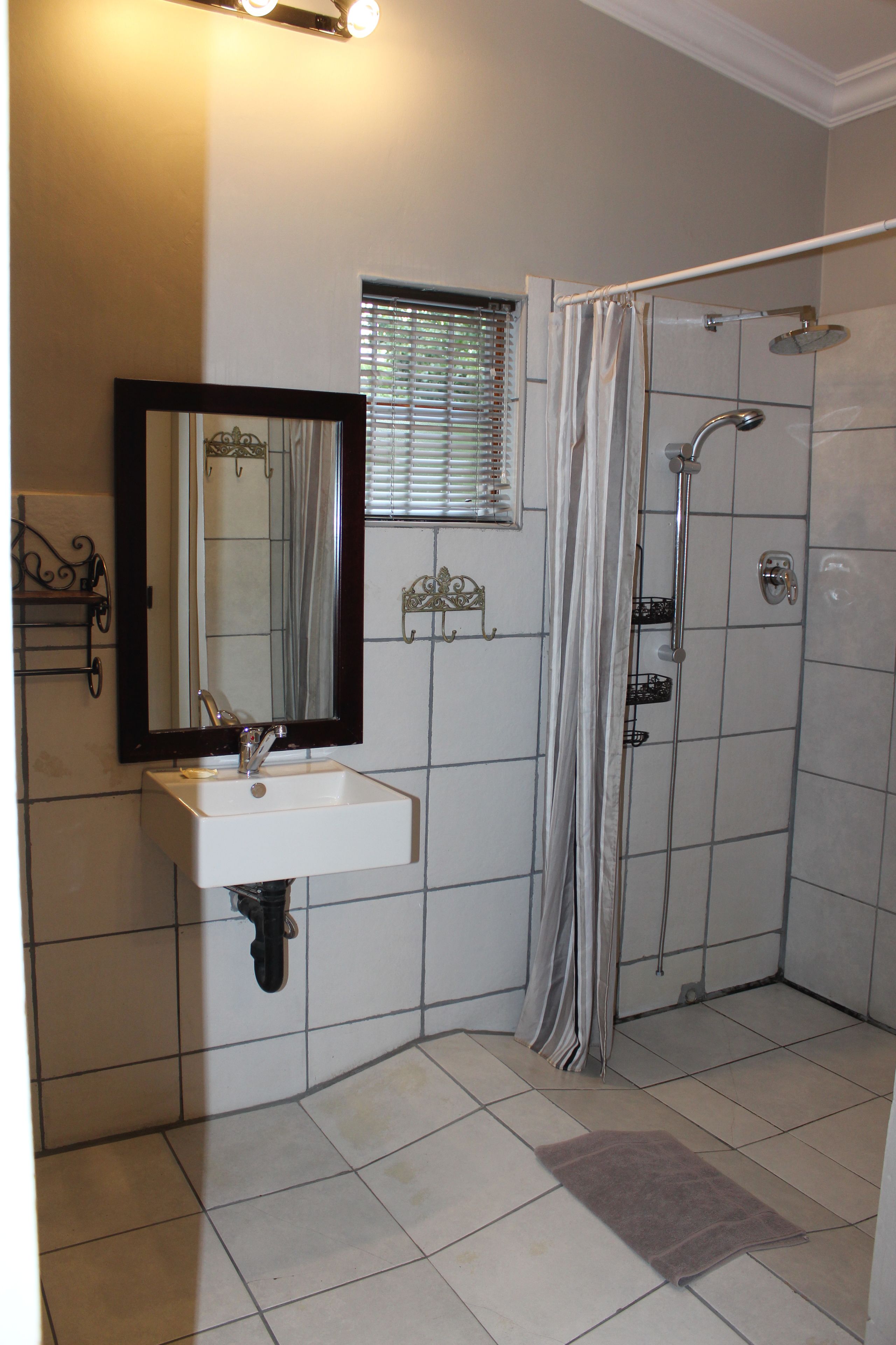 Ein Badezimmer mit Waschbecken, Spiegel, Dusche und Fliesenboden.