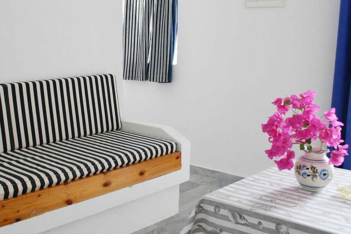 A striped sofa with a wooden base, a vase with pink flowers, and a patterned table.