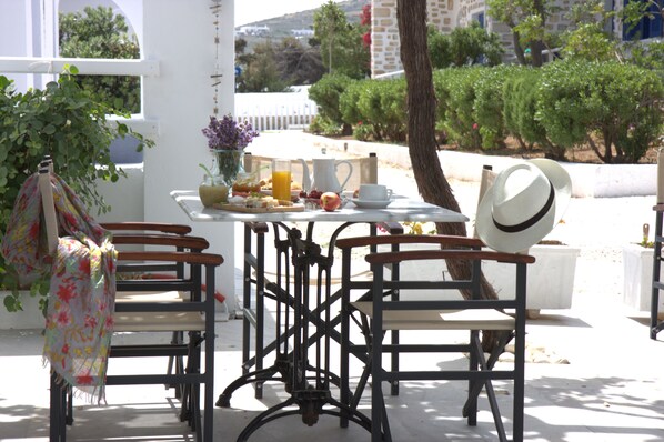 A table set with breakfast items, a white hat, and a bench with a floral cloth. - Bungalows Marina (Paros)