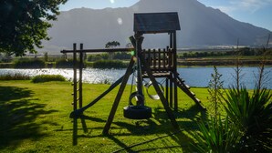 A swing set with a solar panel roof, a tire swing, and a view of a lake and mountains in the background. - Reflections Guest Farm (Tulbagh)