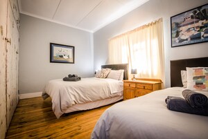 A hotel room with two beds, a wooden dresser, a nightstand, a framed picture, and a window with curtains.