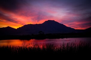 A mountain silhouette at sunset with a calm lake in the foreground.