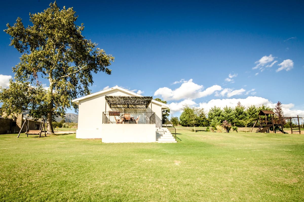 A white building with a balcony, surrounded by a grassy area and trees.
