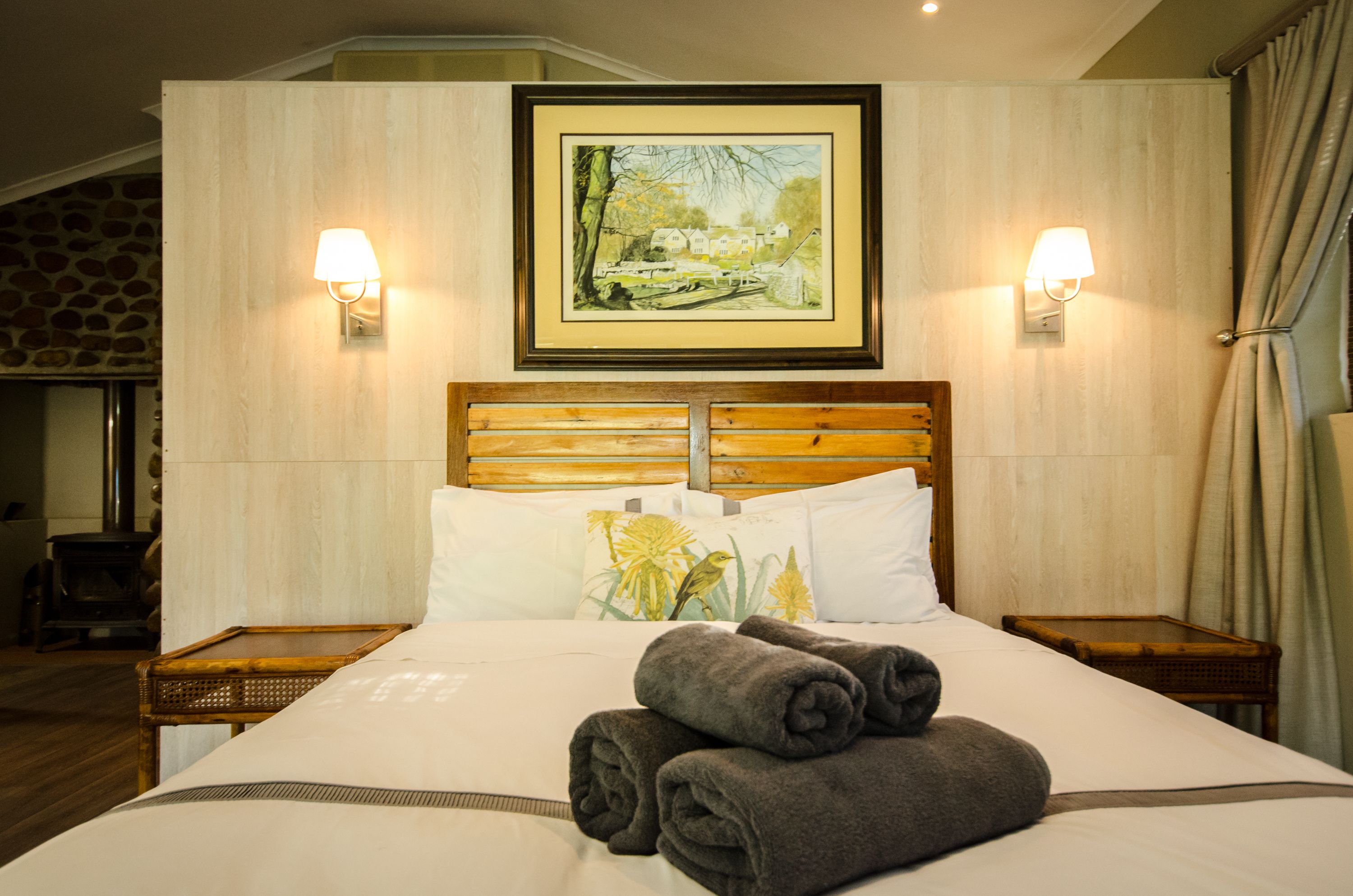 A neatly made bed with a headboard, two bedside tables, and a framed painting above the bed.