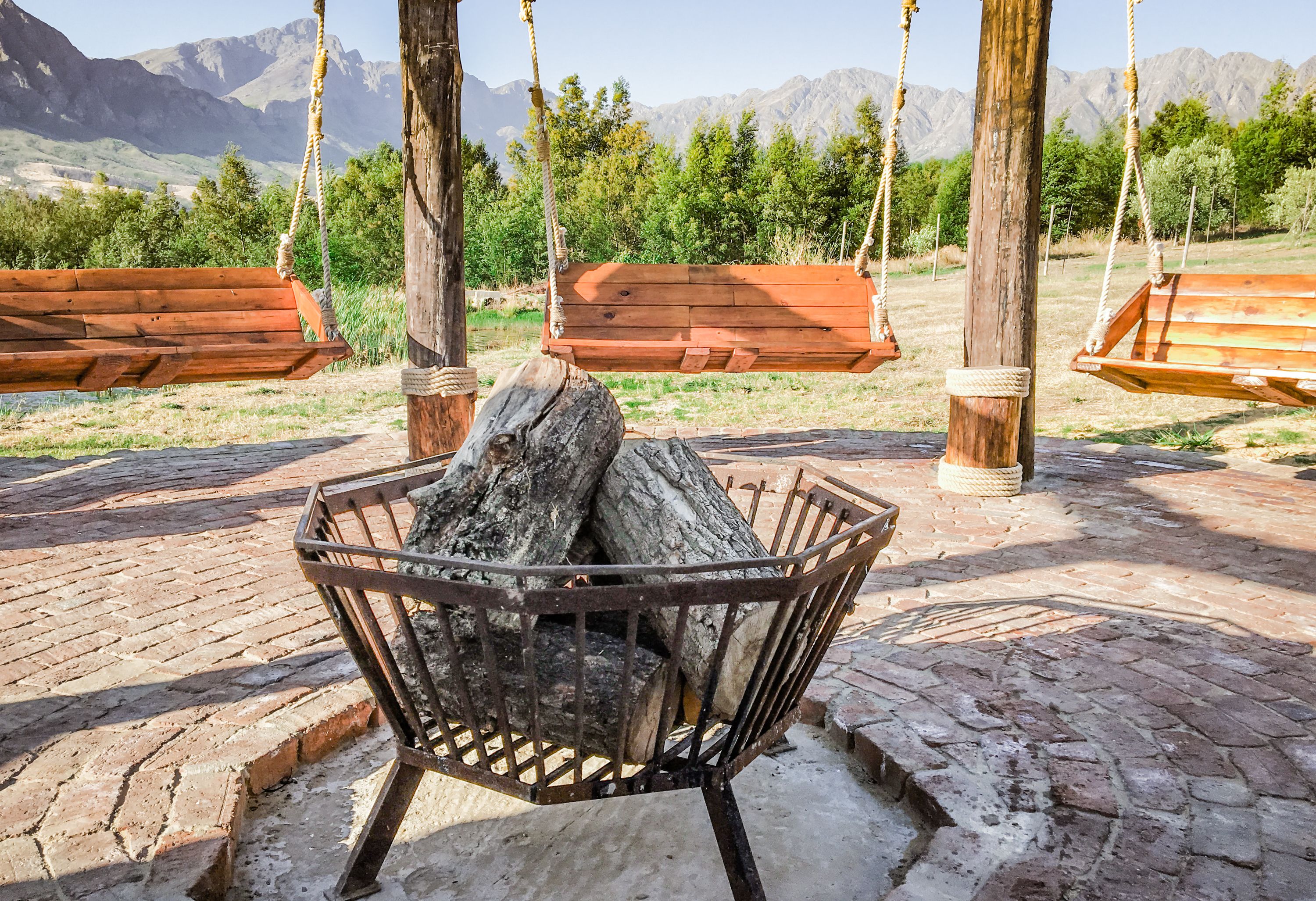 A rustic outdoor seating area with wooden swings and a metal fire pit.