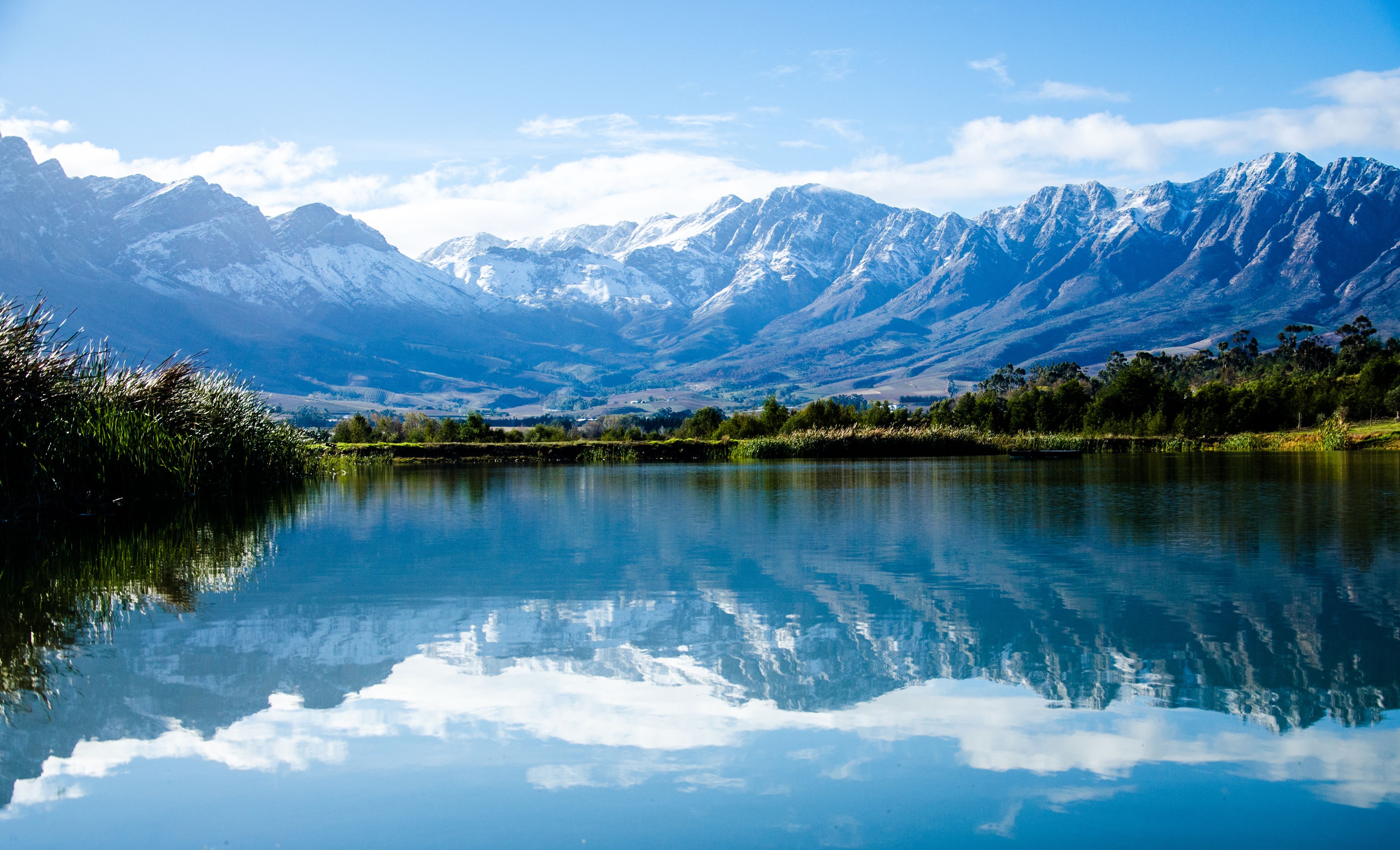A tranquil lake reflecting mountains, surrounded by lush greenery and clear skies.