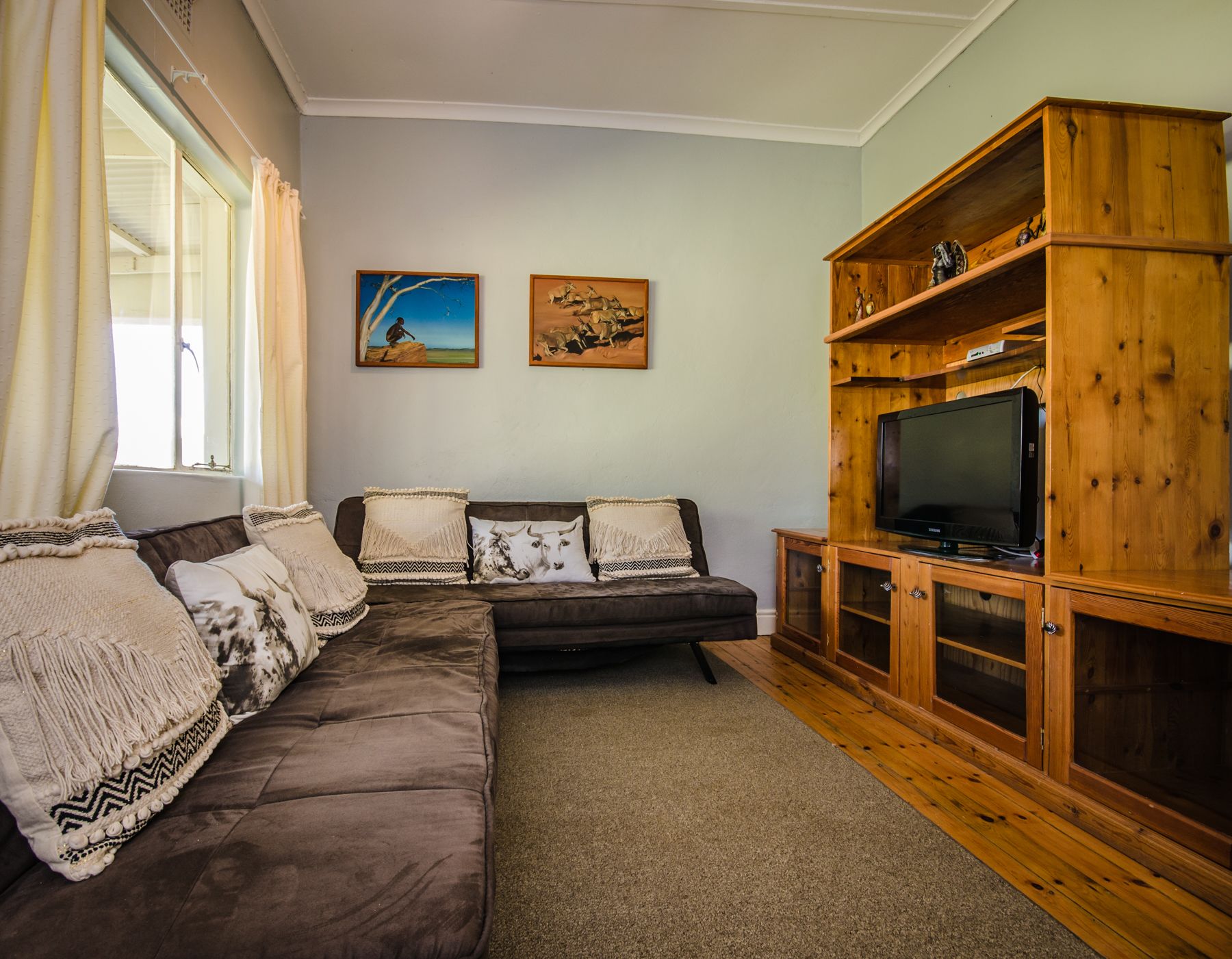 Una sala de estar con un sofá modular, un mueble de entretenimiento de madera con un televisor y dos cuadros colgados en la pared.