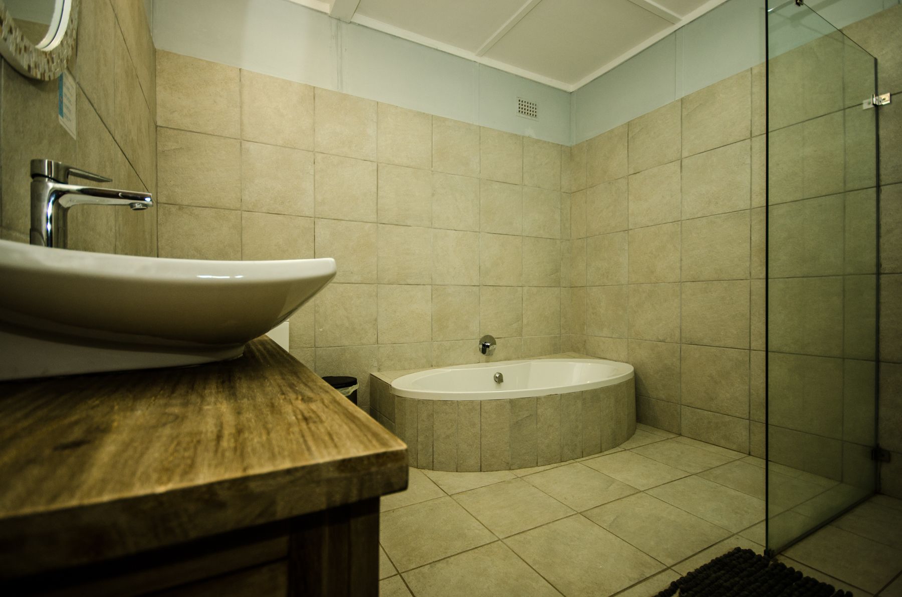 A bathroom with a wooden vanity, a white sink, a bathtub, and a glass shower enclosure.