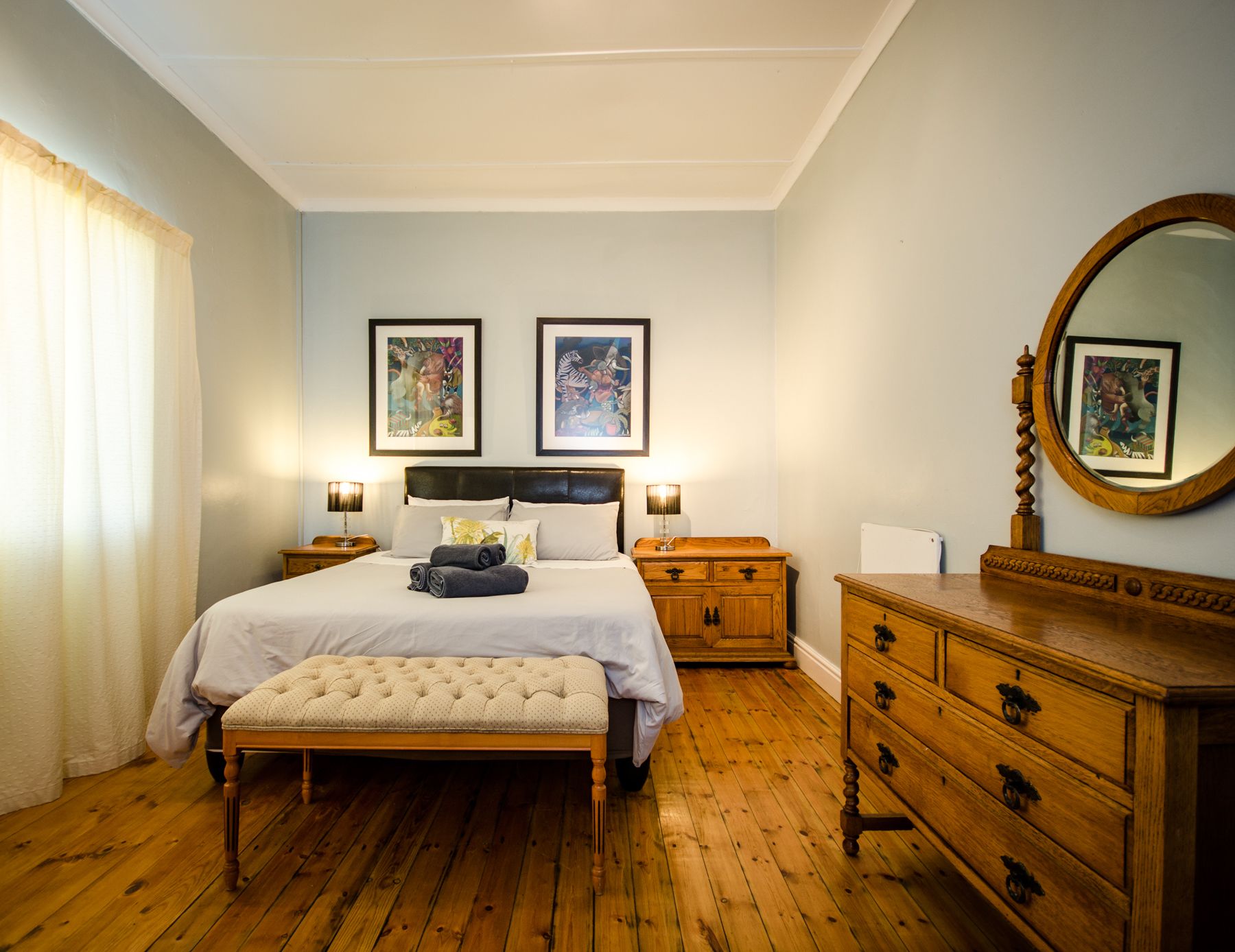 Een slaapkamer met een groot bed, een houten dressoir en twee ingelijste kunstwerken aan de muur.