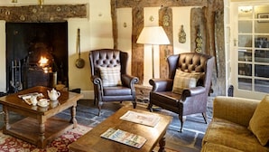 A rustic living room with exposed wooden beams, a fireplace, leather armchairs, and a wooden coffee table.