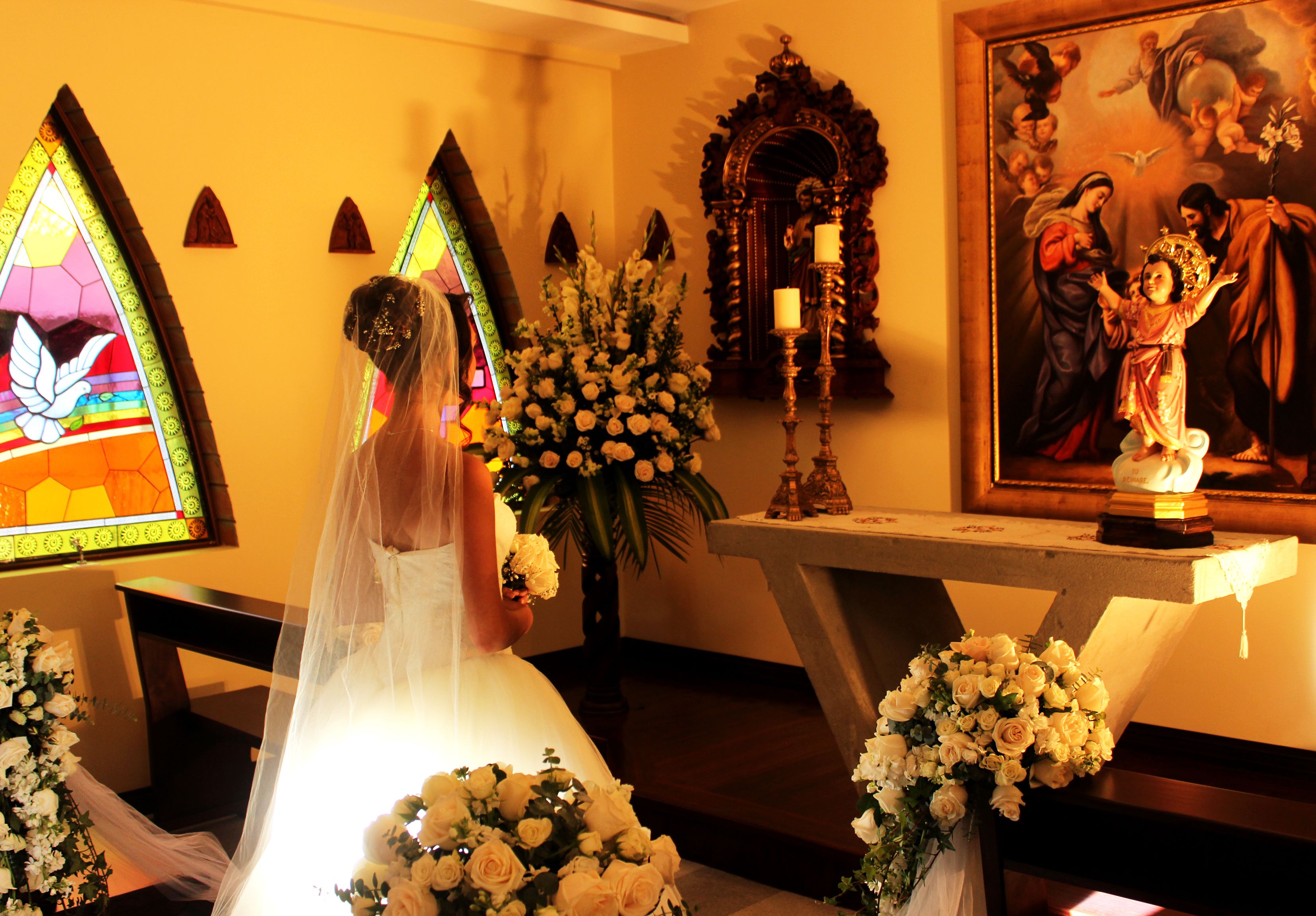 A wedding ceremony in a church with a bride, altar, floral arrangements, and religious paintings.