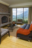 Una sala de estar con chimenea, un sofá, un sillón y vistas a un paisaje montañoso.