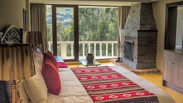 Un dormitorio con una cama grande, una chimenea, un balcón con vistas al campo y una zona de comedor con mesa y sillas.