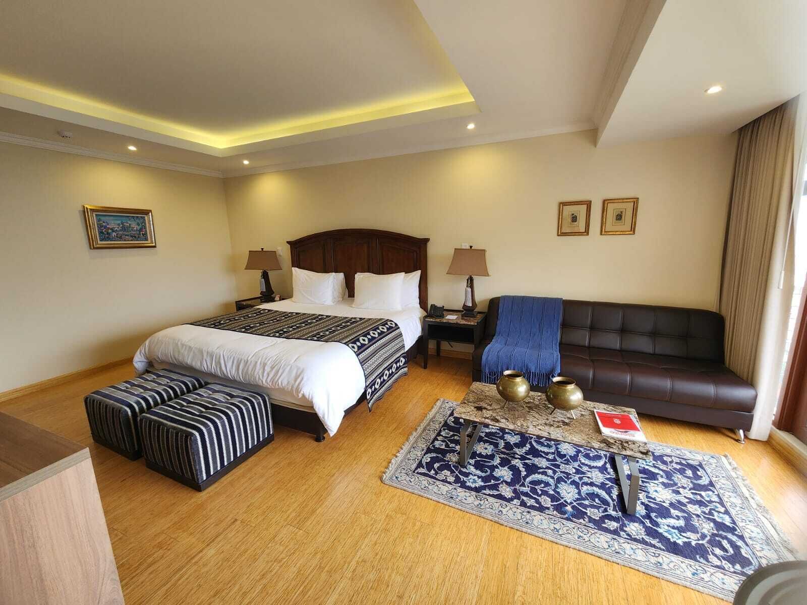 Una habitación de hotel con cama doble, sofá, una mesita con adornos y una alfombra estampada.