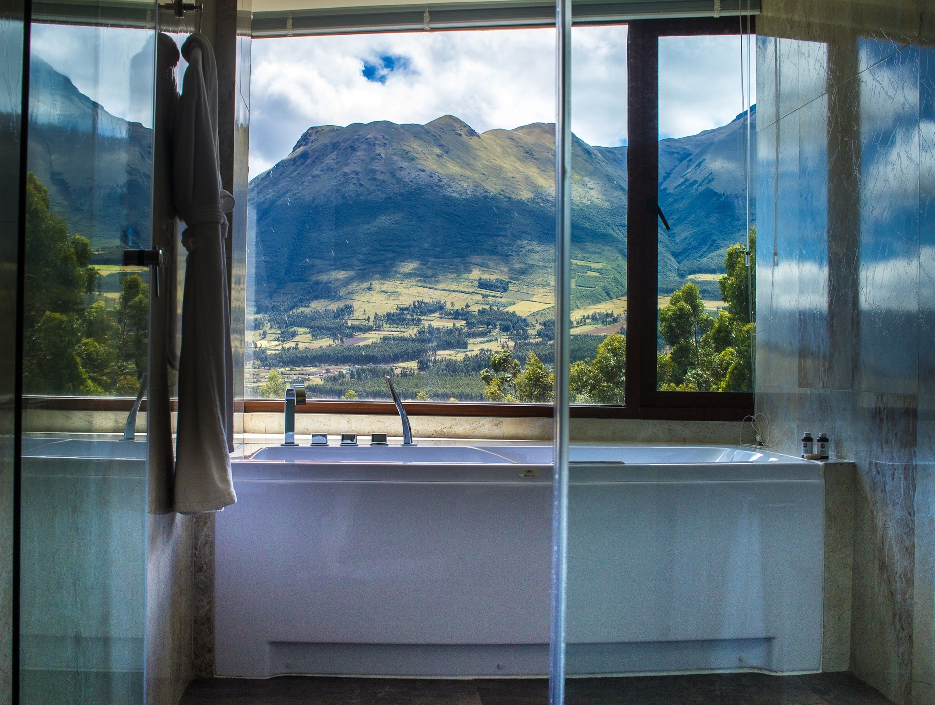 A bathroom with a bathtub, a window with a mountain view, and a towel hanging on the door.