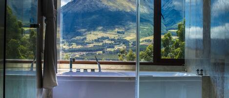 A bathroom with a bathtub, a window with a mountain view, and a towel hanging on the door.